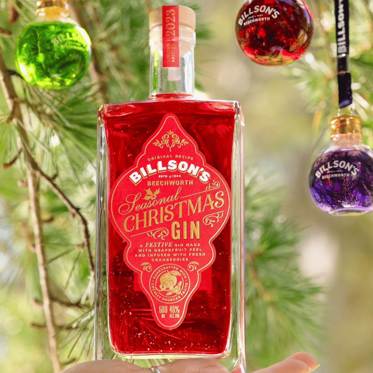 An image of a bottle of Christmas gin held up against a backdrop of a festive tree.