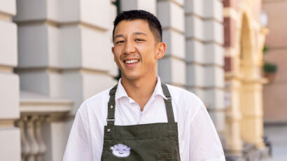 Chef Brendan Pang on the main cooking stage in an apron, smiling while pulling apart dumpling wrapper mix at the Good Food & Wine Show.