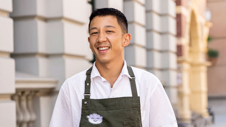 Chef Brendan Pang on the main cooking stage in an apron, smiling while pulling apart dumpling wrapper mix at the Good Food & Wine Show.