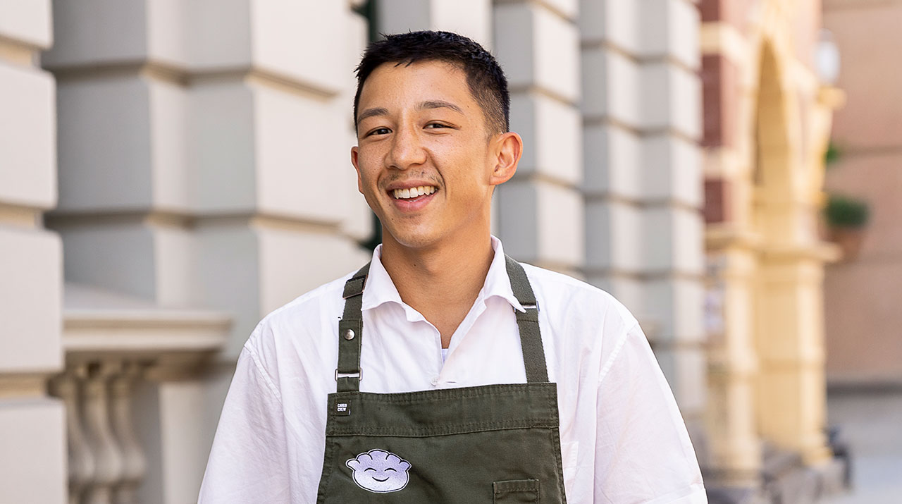 Chef Brendan Pang on the main cooking stage in an apron, smiling while pulling apart dumpling wrapper mix at the Good Food & Wine Show.