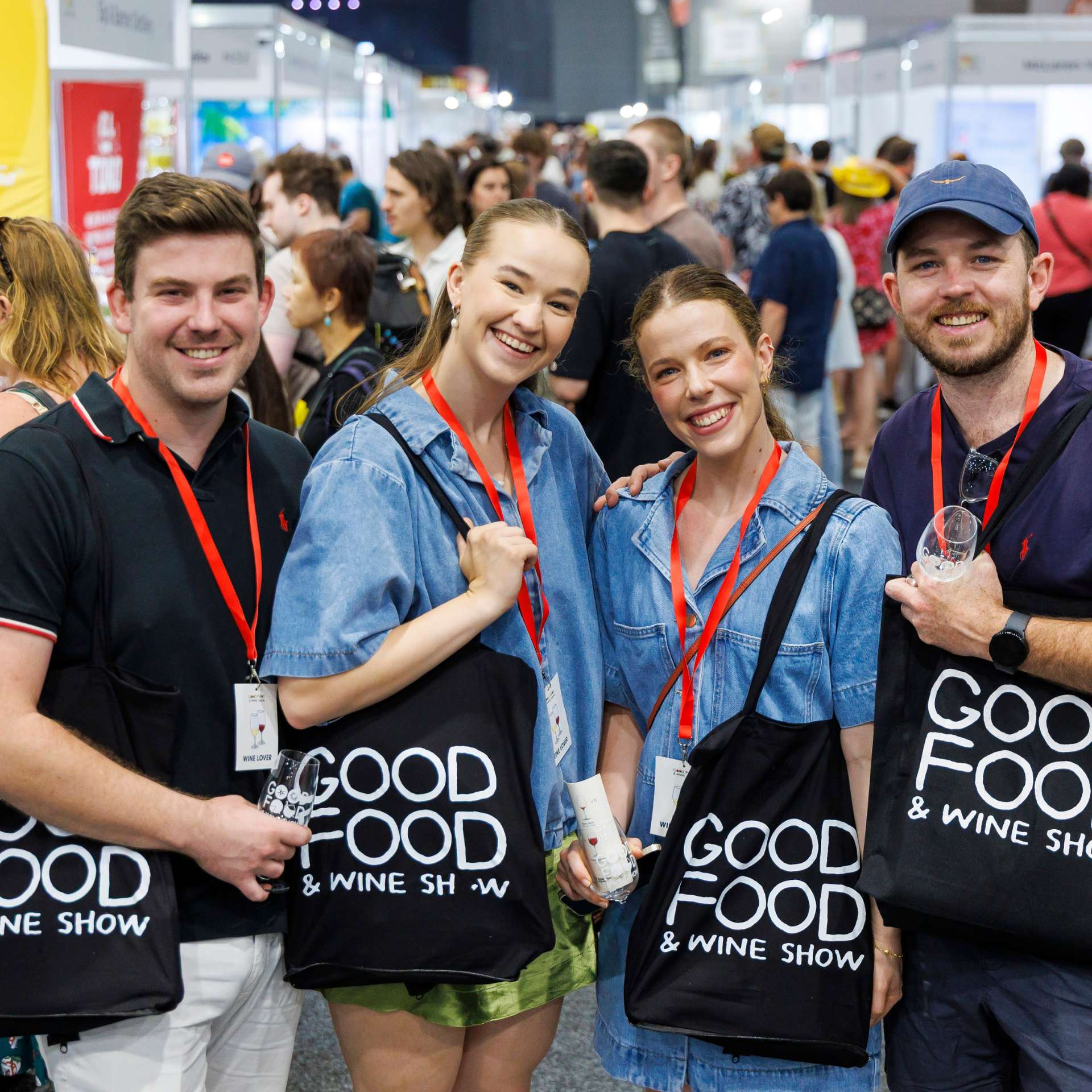 Group of four young adults holding Good Food & Wine Show black tote bags
