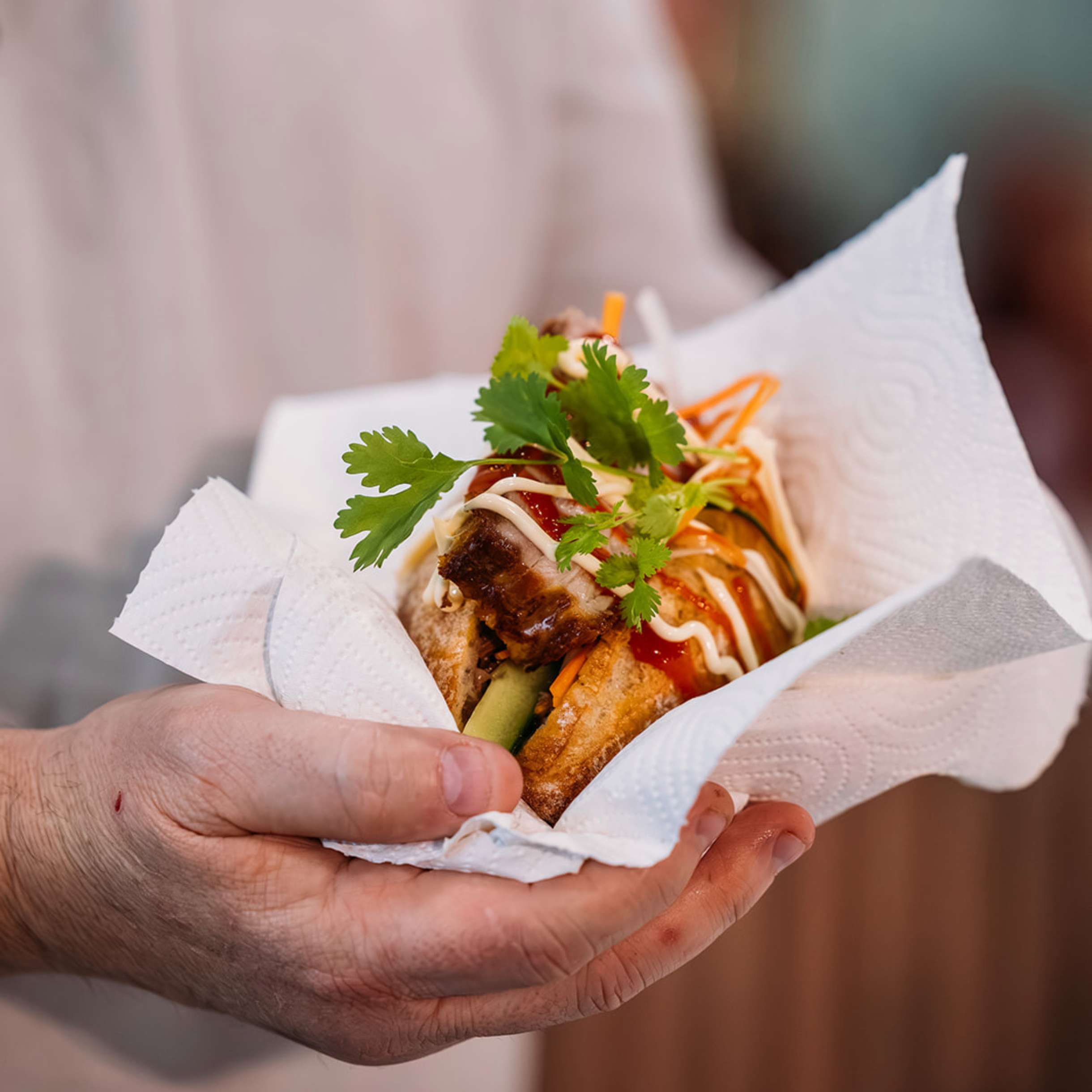 Person holding a pork belly banh mi in a napkin at the Good Food & Wine Show