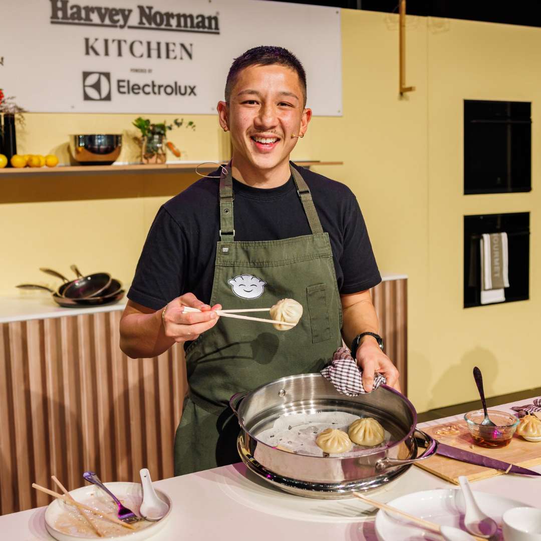 Chef Brendan Pang smiling on stage while presenting freshly made dumplings at the Good Food & Wine Show.