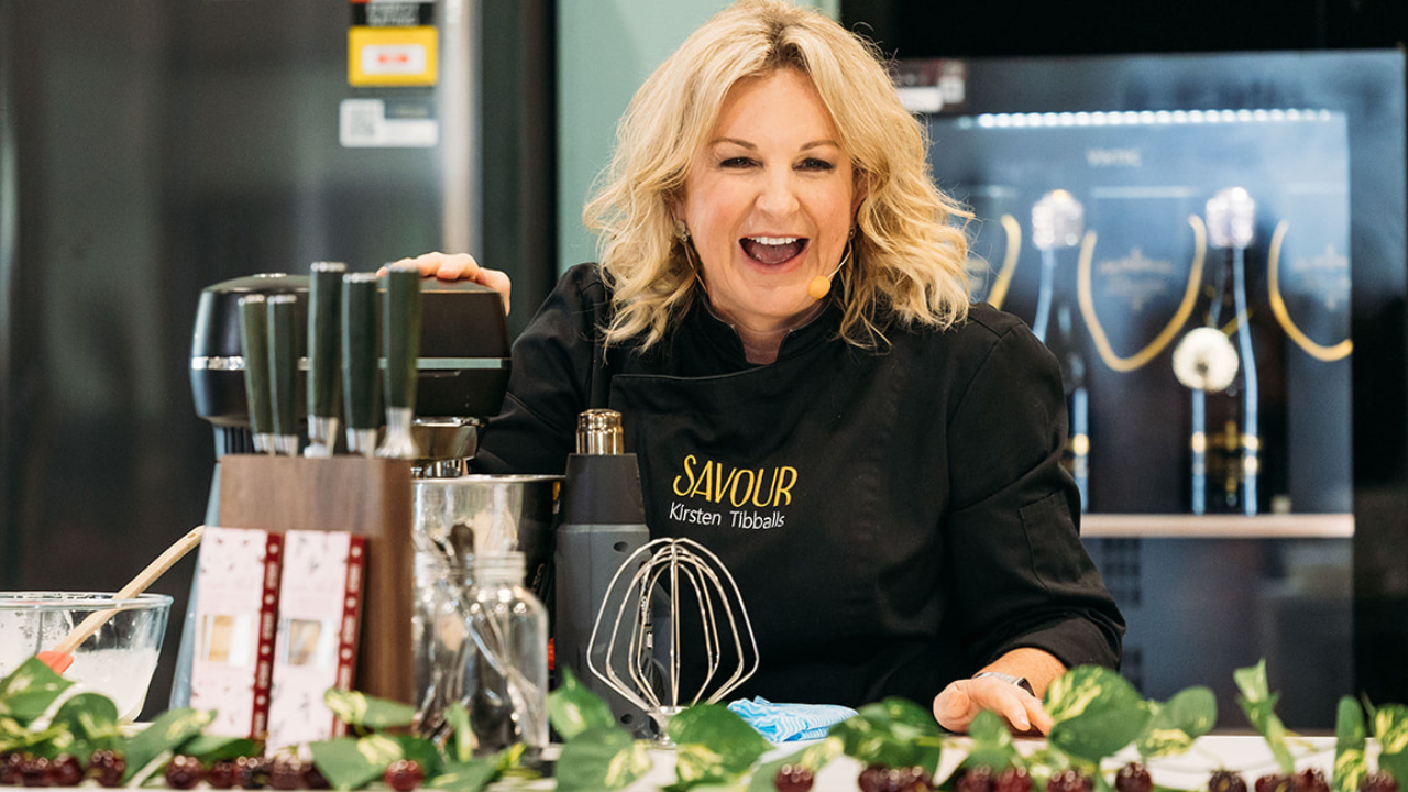 Celebrity pastry chef Kirsten Tibballs laughing on the main stage with a mixer in front of her at the Good Food & Wine Show.