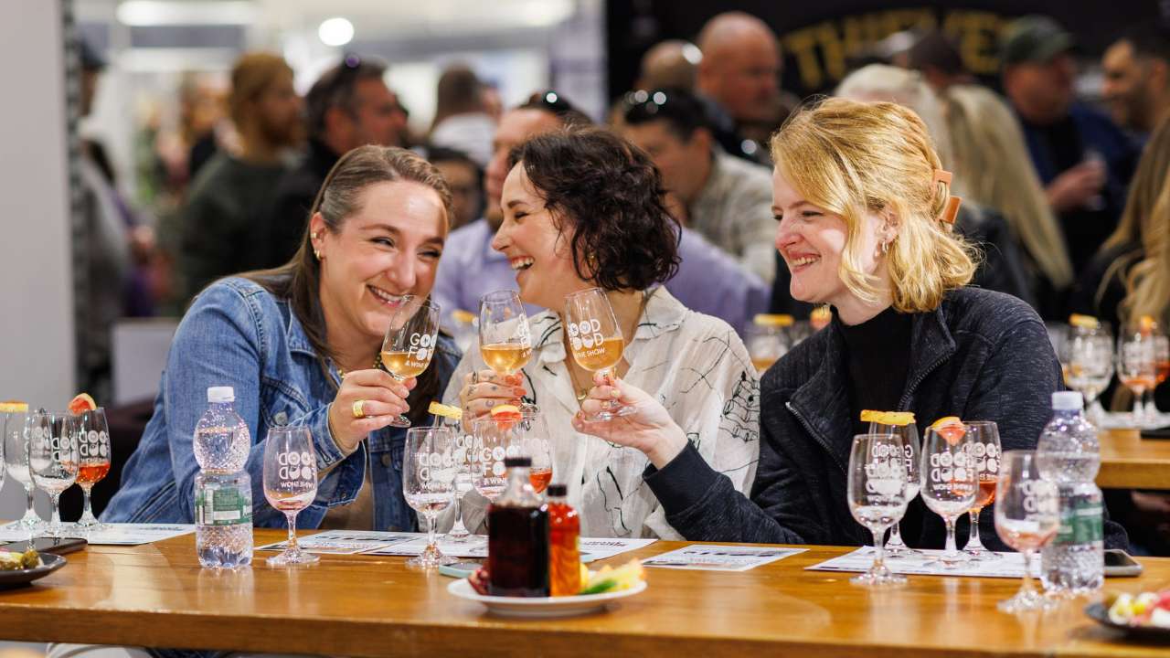 Three women toasting with wine glasses at the Good Food & Wine Show tasting session.