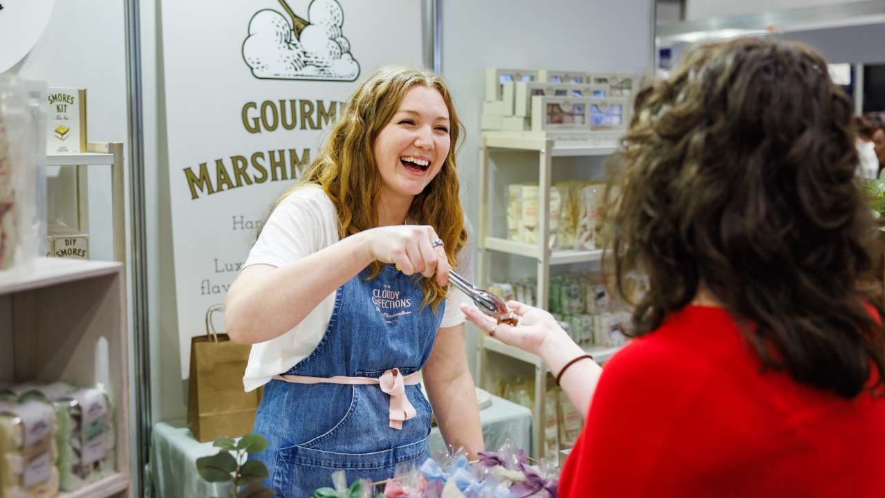 Exhibitor giving a tasting to a smiling customer at the Good Food & Wine Show