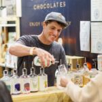 Young man in a hat pouring gin into a customer’s tasting glass at the Good Food & Wine Show