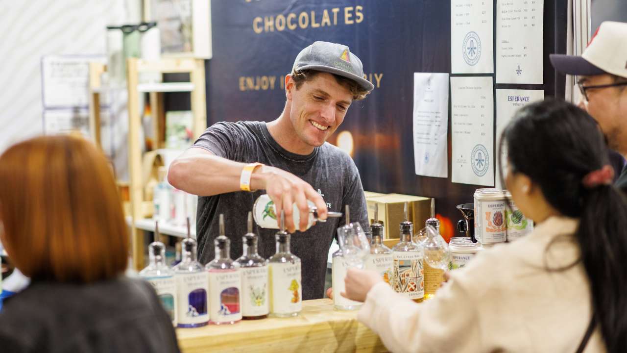 Young man in a hat pouring gin into a customer’s tasting glass at the Good Food & Wine Show