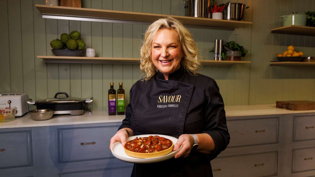 Chef Kirsten Tibballs smiling in a kitchen while holding a freshly made tart.