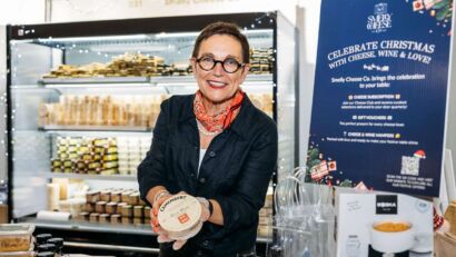 Valerie Henbest, owner of Smelly Cheese Co, smiling at the camera while holding a block of cheese.