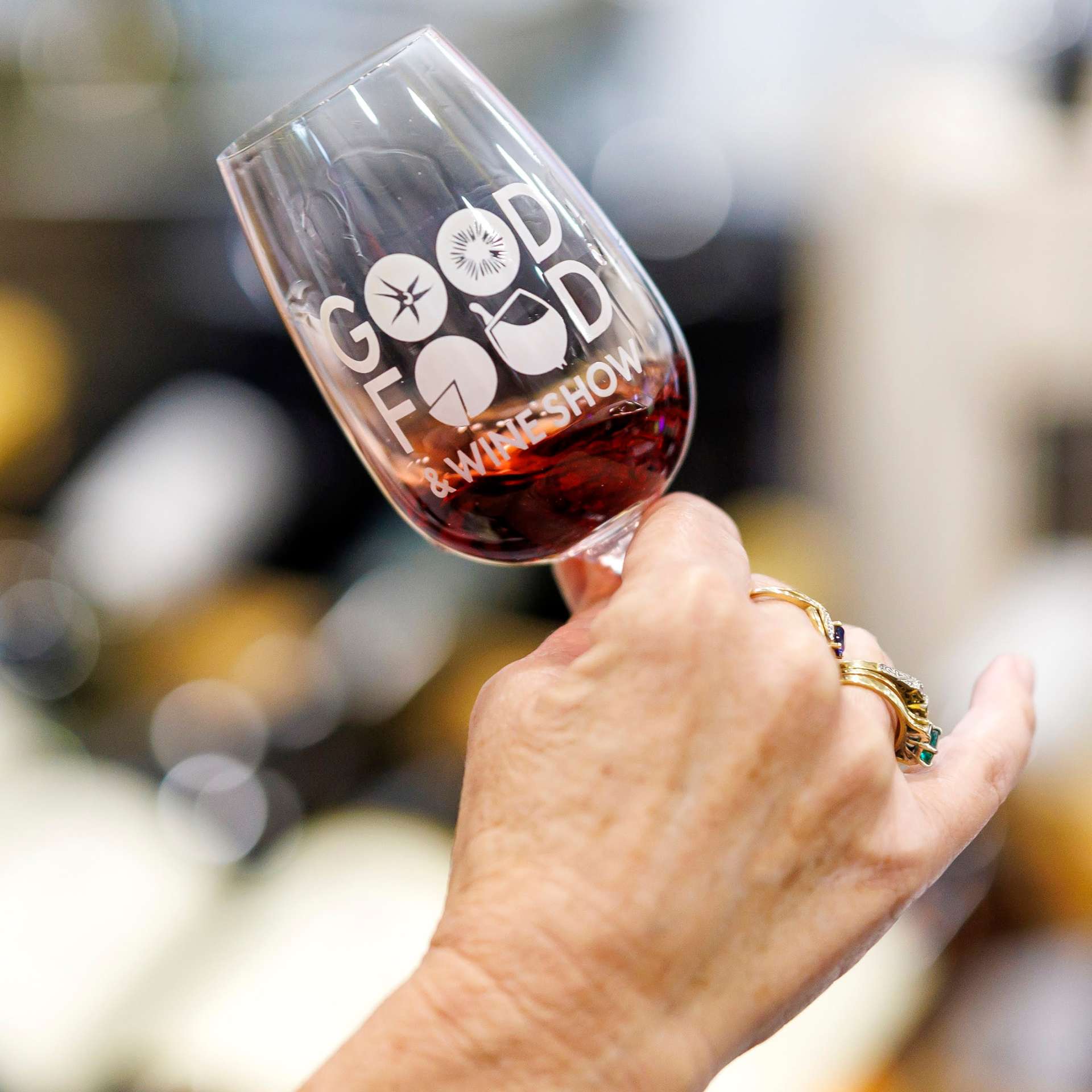 Person holding a Good Food & Wine Show tasting glass filled with red wine