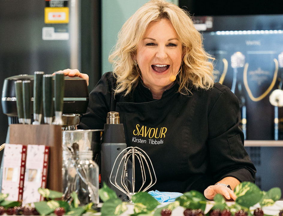 Celebrity pastry chef Kirsten Tibballs laughing on the main stage with a mixer in front of her at the Good Food & Wine Show.