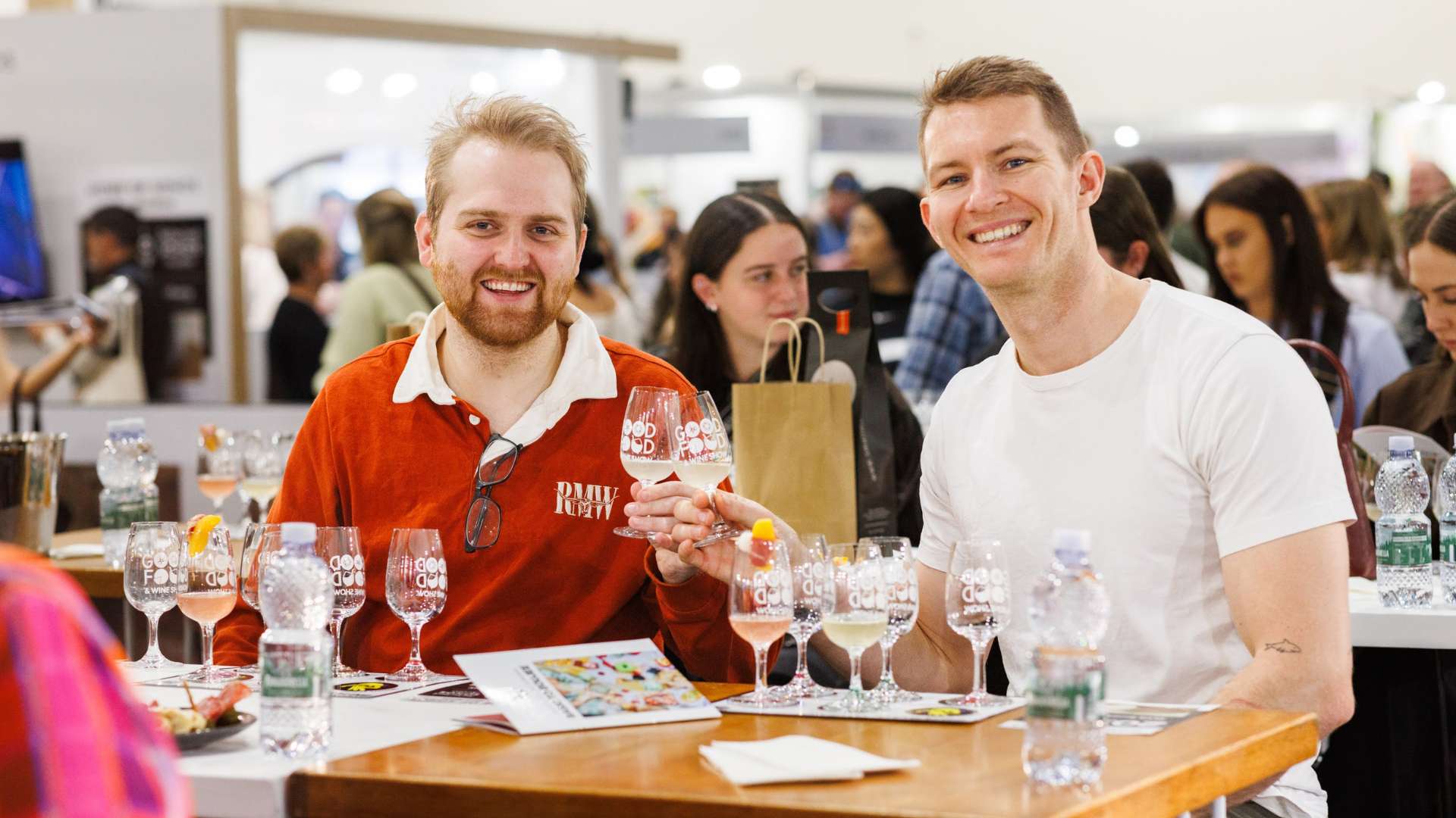 Two men smiling and raising wine glasses during a tasting session at the Good Food & Wine Show.