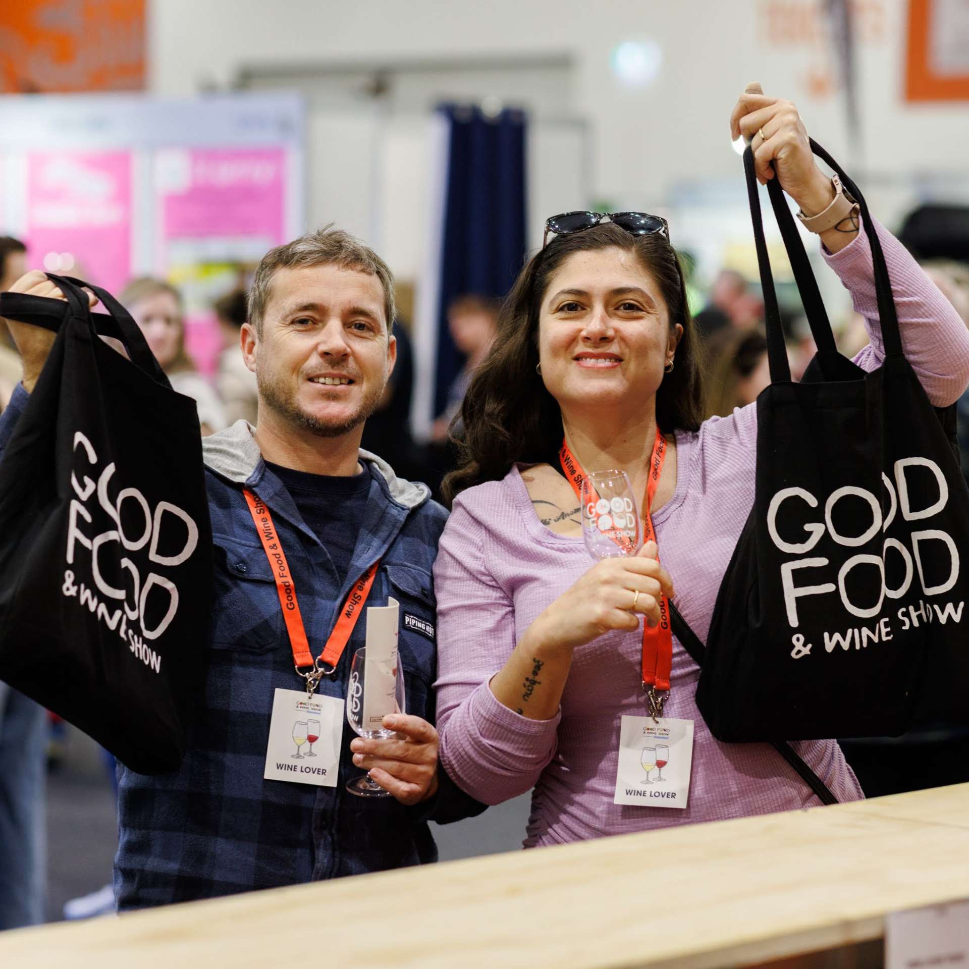Man and woman holding Wine Lover tote bags with lanyards at the Good Food & Wine Show