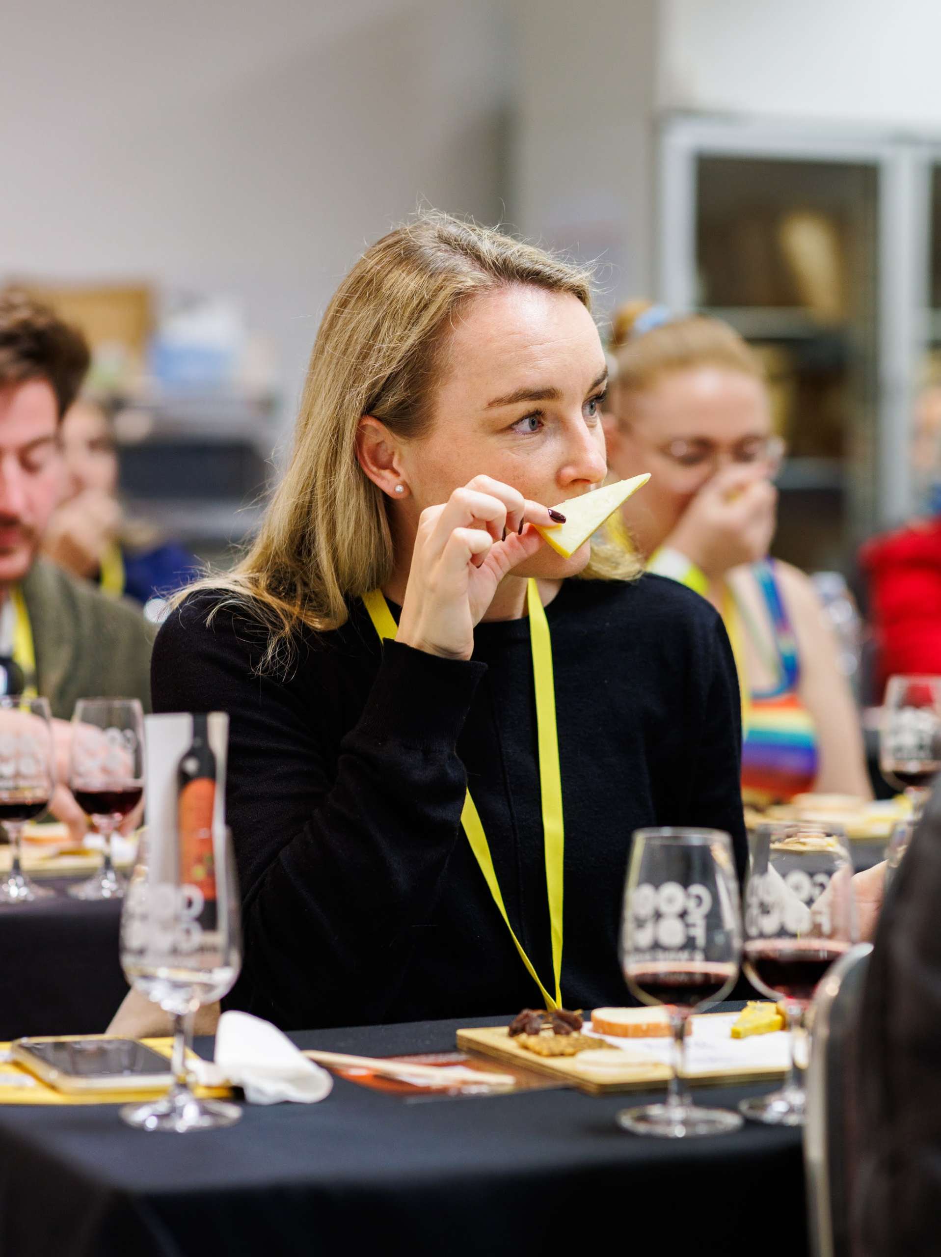 Attendee tasting cheese during a Cheese Lover Masterclass at the Good Food & Wine Show, seated at a tasting table with wine glasses.