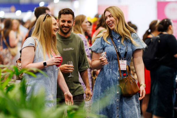 Three visitors raise their glasses and smile, enjoying the tasting experiences at the Good Food & Wine Show.