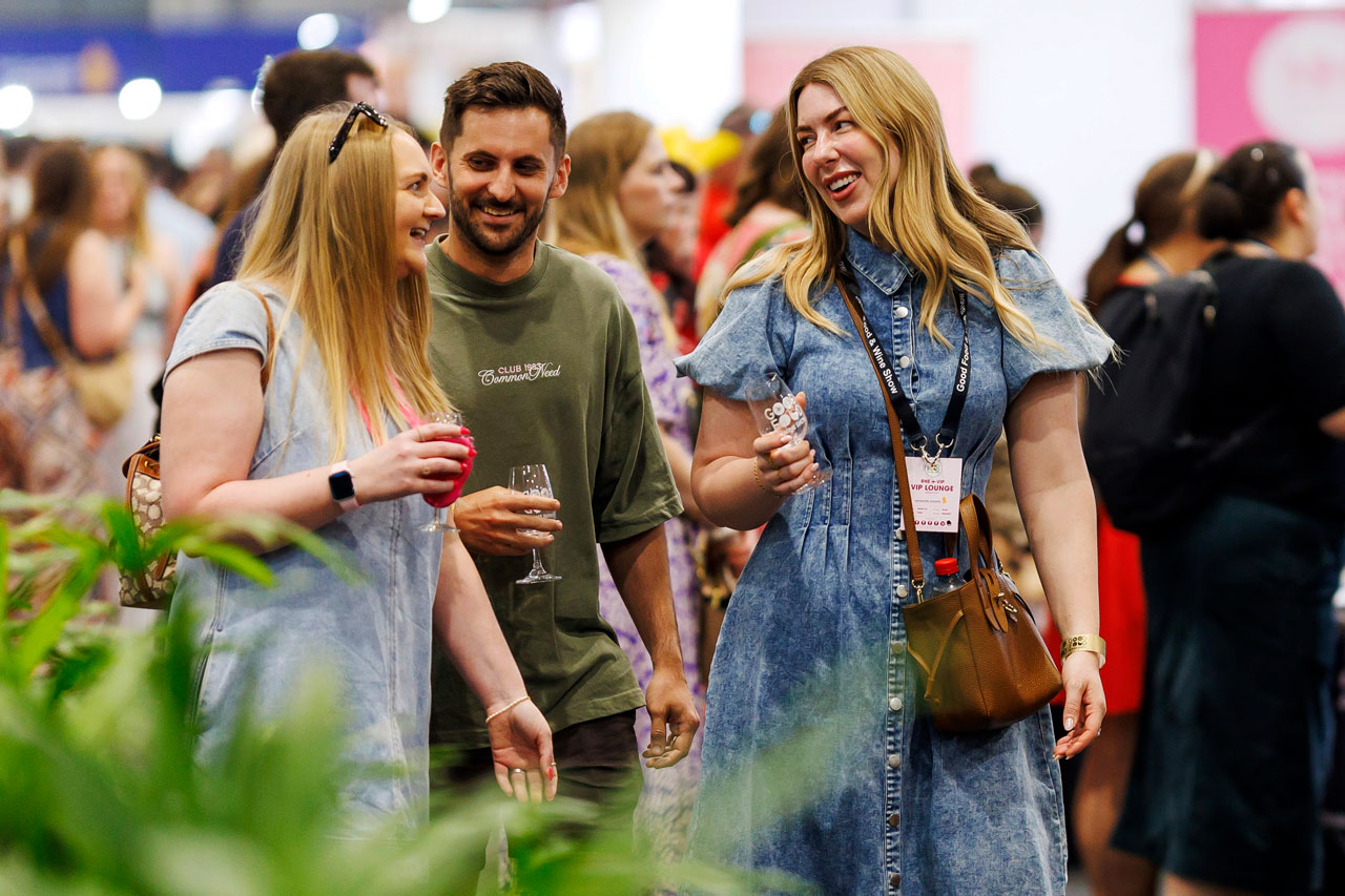Three visitors raise their glasses and smile, enjoying the tasting experiences at the Good Food & Wine Show.