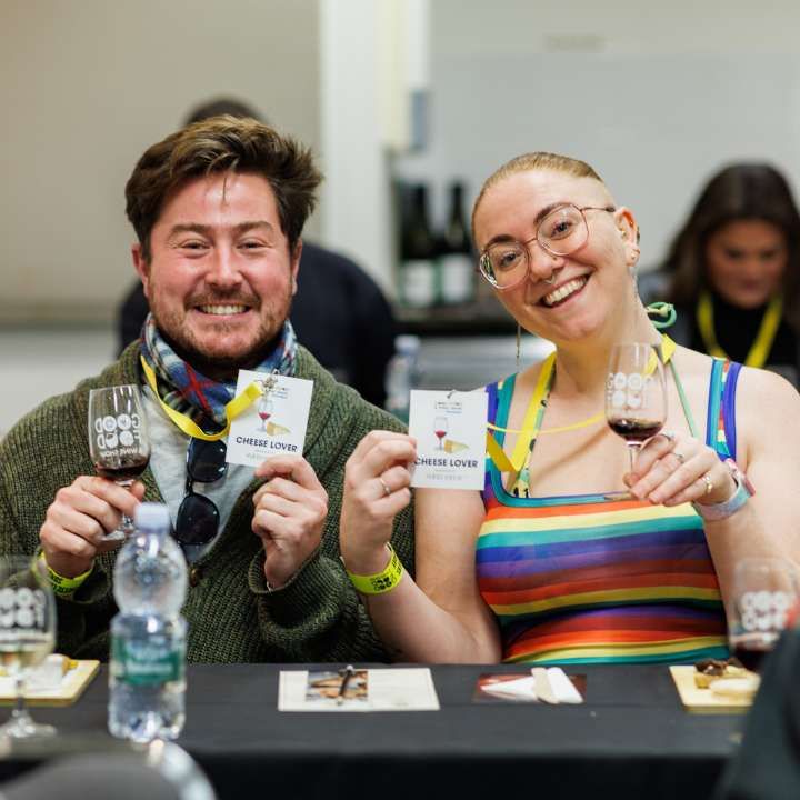 Two attendees holding wine glasses and Cheese Lover lanyards during a Cheese, Wine & Tunes class at the Good Food & Wine Show.